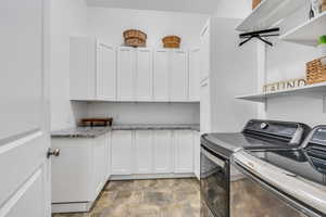 Laundry room with cabinet space, independent washer and dryer, and stone finish floor