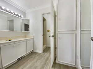 Full bathroom featuring vanity, wood finished floors, baseboards, and ornamental molding