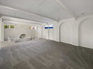 Unfurnished living room with beamed ceiling, carpet flooring, brick wall, and baseboards