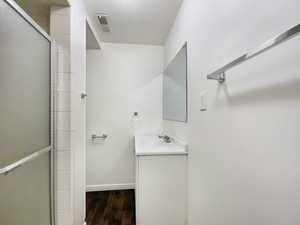 Full bathroom with vanity, wood finished floors, visible vents, baseboards, and an enclosed shower