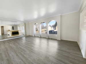 Unfurnished living room with a fireplace, crown molding, baseboards, and wood finished floors