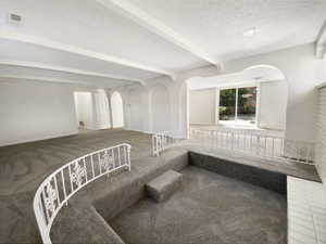 Interior space featuring carpet, visible vents, beam ceiling, arched walkways, and a textured ceiling