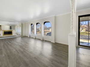 Unfurnished living room featuring visible vents, wood finished floors, a glass covered fireplace, crown molding, and baseboards