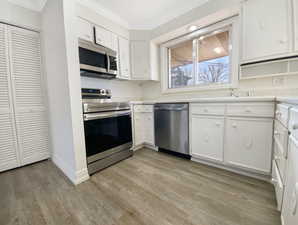 Kitchen with ornamental molding, white cabinetry, light wood-style floors, appliances with stainless steel finishes, and light countertops