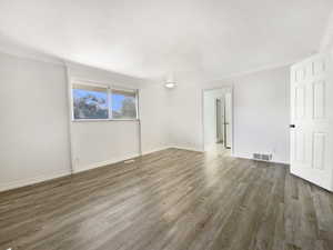 Unfurnished room featuring visible vents, baseboards, wood finished floors, and ornamental molding