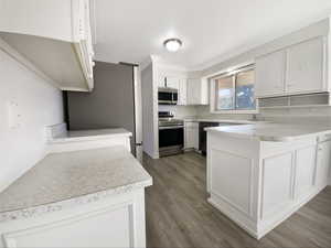 Kitchen with light countertops, appliances with stainless steel finishes, a peninsula, wood finished floors, and white cabinetry