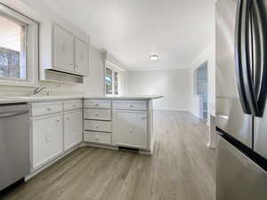 Kitchen with ornamental molding, light countertops, white cabinets, light wood-style floors, and appliances with stainless steel finishes