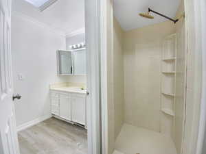 Full bathroom featuring wood finished floors, a tile shower, crown molding, baseboards, and vanity