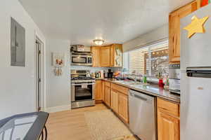 Kitchen featuring light wood finished floors, electric panel, appliances with stainless steel finishes, a textured ceiling, and a sink