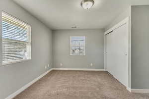 Unfurnished bedroom featuring carpet flooring, multiple windows, baseboards, and visible vents