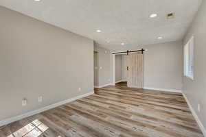 Spare room with baseboards, visible vents, light wood finished floors, recessed lighting, and a barn door