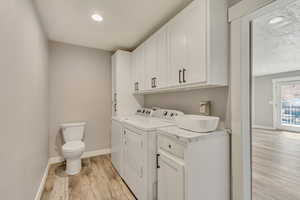 Laundry area with light wood finished floors, a sink, baseboards, laundry area, and separate washer and dryer