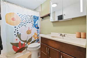 Bathroom with a shower with curtain, a textured ceiling, vanity, and toilet