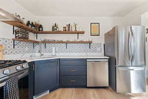 Kitchen with open shelves, appliances with stainless steel finishes, light countertops, and a sink