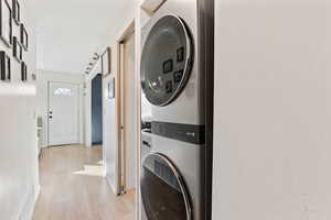 Washroom with light wood finished floors, stacked washer / dryer, visible vents, a barn door, and laundry area