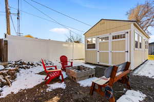 Snow covered structure featuring a storage unit, an outdoor structure, and fence