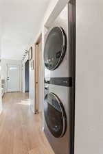 Laundry room with baseboards, stacked washing maching and dryer, laundry area, light wood-style floors, and a textured wall