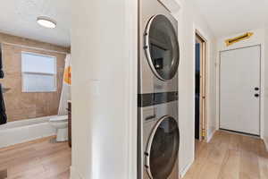 Laundry room featuring light wood finished floors, a textured ceiling, laundry area, and stacked washing maching and dryer