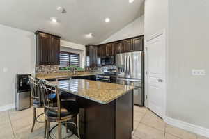 Kitchen with stainless steel appliances, light stone countertops, dark brown cabinetry, and a kitchen island