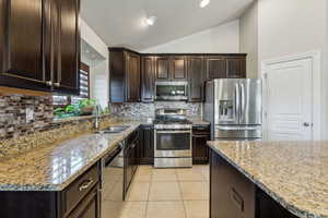 Kitchen featuring dark brown cabinetry, lofted ceiling, light tile patterned floors, appliances with stainless steel finishes, and a sink