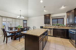 Kitchen with a sink, light stone counters, dark brown cabinetry, appliances with stainless steel finishes, and light tile patterned floors