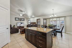 Kitchen with light tile patterned floors, light stone counters, ceiling fan with notable chandelier, and lofted ceiling