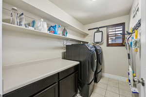 Clothes washing area with light tile patterned floors, baseboards, cabinet space, and washer and clothes dryer