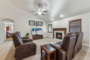 Living area featuring arched walkways, light tile patterned floors, baseboards, ceiling fan, and a tile fireplace