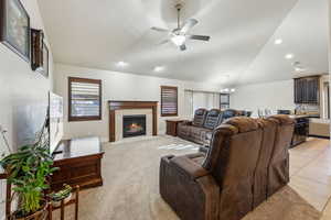 Living area featuring light tile patterned floors, vaulted ceiling, light carpet, a tiled fireplace, and ceiling fan with notable chandelier