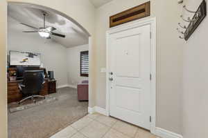 Home office featuring light carpet, a ceiling fan, arched walkways, light tile patterned floors, and lofted ceiling