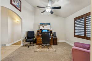 Carpeted home office with vaulted ceiling, visible vents, arched walkways, and baseboards