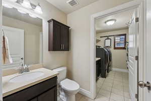 Bathroom with washing machine and clothes dryer, visible vents, tile patterned floors, and vanity