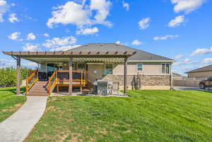 Rear view of property featuring fence, a wooden deck, a yard, stucco siding, and stone siding