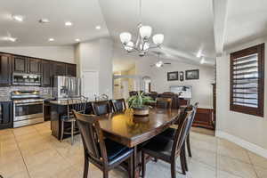 Dining area featuring lofted ceiling, ceiling fan with notable chandelier, arched walkways, light tile patterned floors, and baseboards