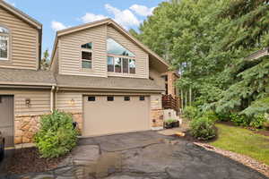 View of front facade featuring an attached garage, asphalt driveway, stone siding, and roof with shingles
