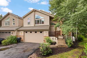 View of front of home with a garage, asphalt driveway, stone siding, and a shingled roof