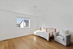 Bedroom with visible vents, a textured ceiling, baseboards, and wood finished floors