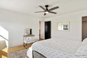 Bedroom with wood finished floors, a closet, baseboards, attic access, and ceiling fan