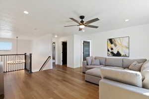 Living room with ceiling fan with notable chandelier, recessed lighting, wood finished floors, and baseboards