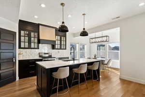 Kitchen with stainless steel electric stove, a kitchen island with sink, a sink, light countertops, and tasteful backsplash