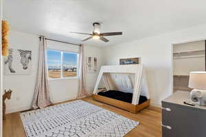 Bedroom with a ceiling fan, baseboards, light wood finished floors, a closet, and a textured ceiling