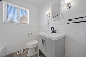 Bathroom featuring vanity, wood finished floors, visible vents, tile walls, and toilet