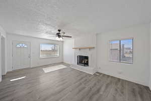 Unfurnished living room with a brick fireplace, wood finished floors, visible vents, and a wealth of natural light