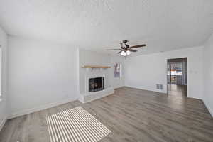 Unfurnished living room with visible vents, a fireplace, baseboards, and wood finished floors