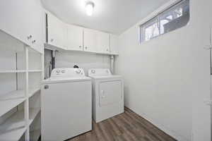 Clothes washing area featuring washer and dryer, cabinet space, and dark wood-style flooring