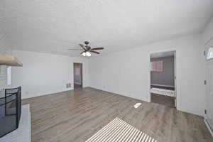 Unfurnished living room with visible vents, ceiling fan, baseboards, a fireplace, and wood finished floors