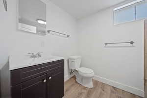 Bathroom featuring toilet, a textured ceiling, wood finished floors, baseboards, and vanity