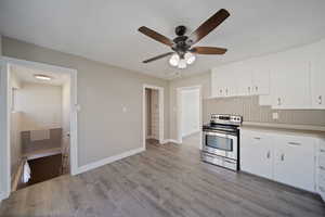 Kitchen featuring electric range, white cabinetry, light wood-style floors, light countertops, and baseboards