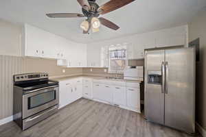 Kitchen with open shelves, a sink, stainless steel appliances, light countertops, and light wood-type flooring