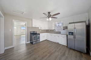 Kitchen featuring dark wood-style flooring, white cabinets, stainless steel appliances, and a sink